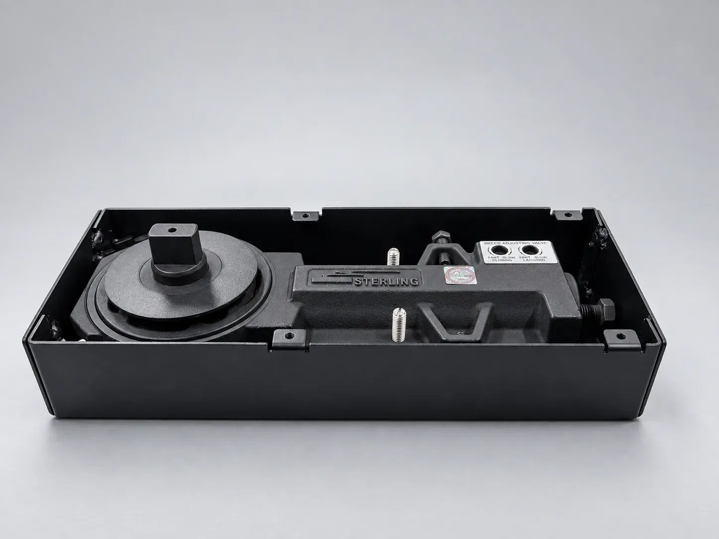Sterling FS 1000 floor spring with its cast body and speed adjusting valve inside a black box, cover plate removed, front view from above, studio photograph