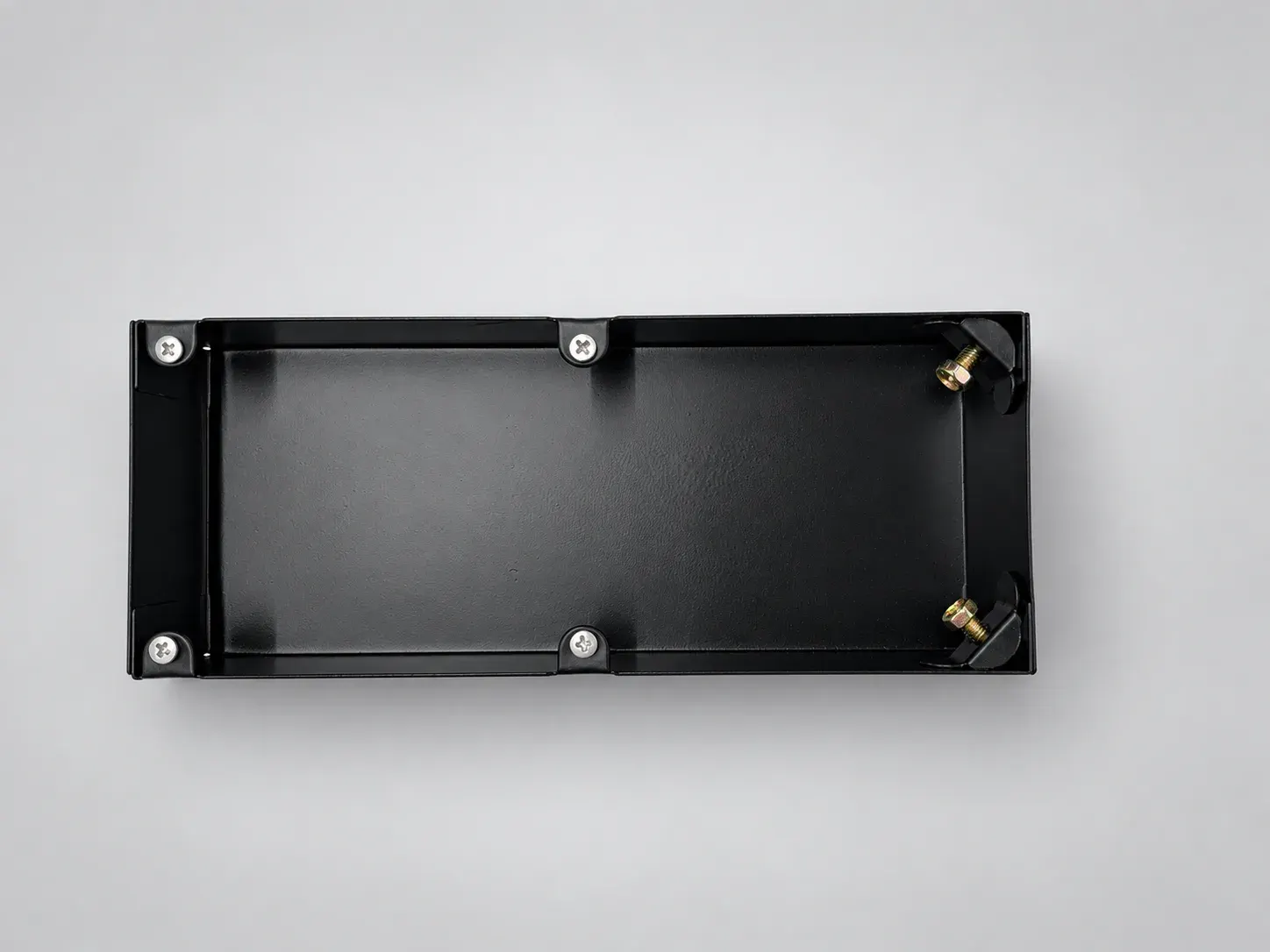Empty black floor spring box with gold-coloured adjusting bolts at one end, overhead view, studio photograph